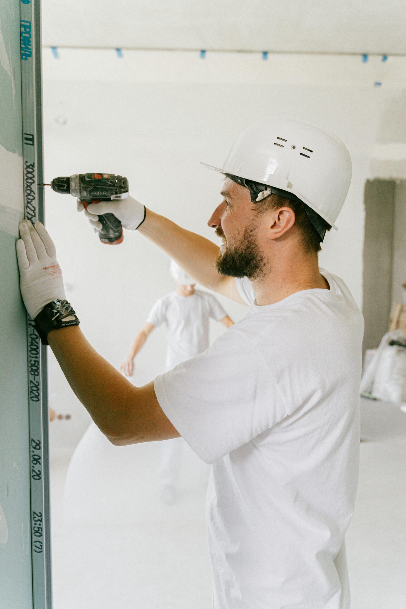 Adult male in safety gear using a power drill on a construction site indoors.