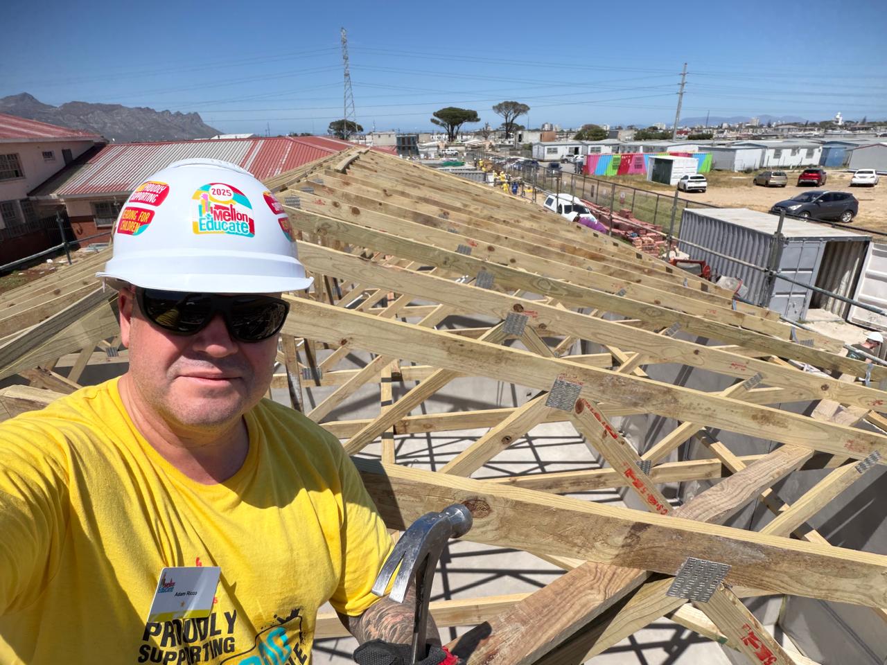 Adam Riccio in a Mellon Educate hard hat on the roof structure of a school build in South Africa
